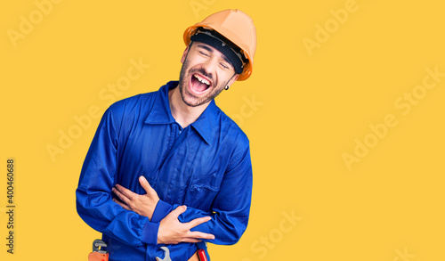 Young hispanic man wearing worker uniform smiling and laughing hard out loud because funny crazy joke with hands on body.