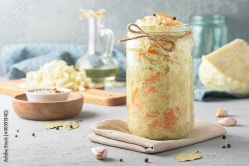 Sauerkraut in a glass jar with ingredients on a concrete background.