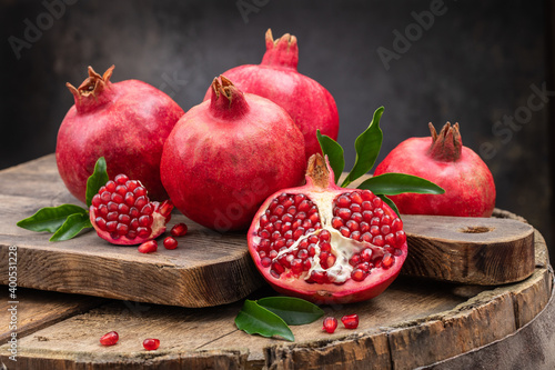 Healthy pomegranate fruit with leaves and open pomegranate on an old wooden board, side view, dark vintage background.