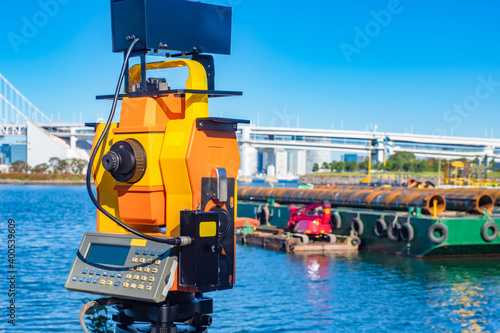 Orange theodolite in close-up. Theodolite with a camera on the background of the pier under construction. Geodesy and cartography. Laser level with camera to record measurement results.