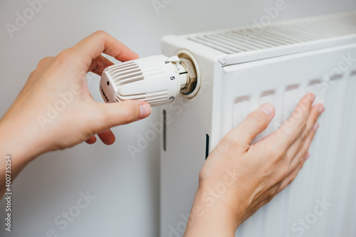 Close up shot of Caucasian female's hand adjusting radiator temperature using thermostat. Home with central heating.