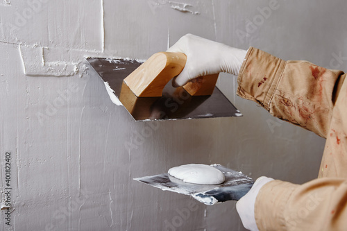 Close up of construction worker plastering and smoothing wall with trowel and putty knife.