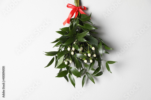 Mistletoe bunch with red bow hanging on white wall. Traditional Christmas decor