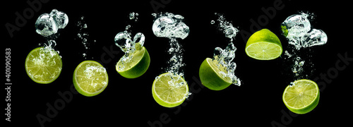 Bunch of lime fruits halves sinking with bubbles into water isolated against black background. Citrus theme, panorama