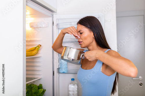 Bad Food In Fridge, young woman in holding her nose because of bad smell from food in refrigerator at home. Unpleasant Smellfrom food gone bad