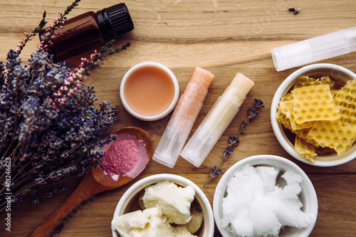 Ingredients for homemade lip balm: shea butter, essential oil, mineral color powder, beeswax, coconut oil. Homemade lip balm lipstick mixture with ingredients scattered around.