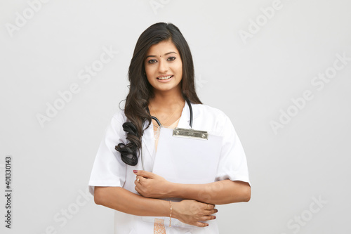 Smiling Indian female doctor greeting with clipboard against white.