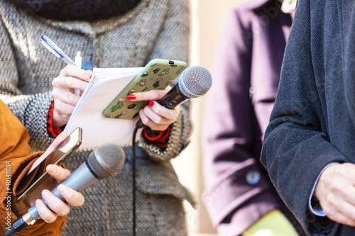 News reporter or TV journalist at press conference, holding microphone and writing notes