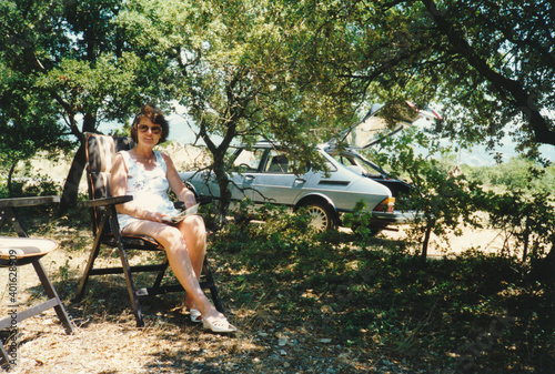 Vintage 1980s image, young woman driving a blue Saab 900 enjoying a picnic on the side of the road.