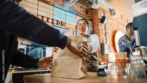 Beautiful Happy Latin Barista Serves Order to a Food Delivery Courier Picking Up Paper Bag with Pastries from a Cafe Restaurant. Delivery Guy Puts Food in His Hot Thermal Insulated Bag.