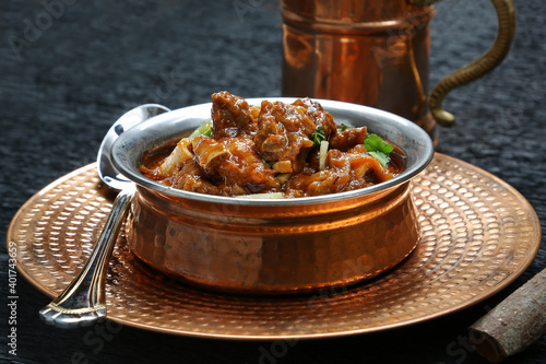 Pakistani famous North Indian curry lamb gosht mutton nirahi karahi kadai bronze bowl black background garnished with chilly 