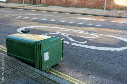 A green recycling wheelie bin blow into the road on a street after high winds