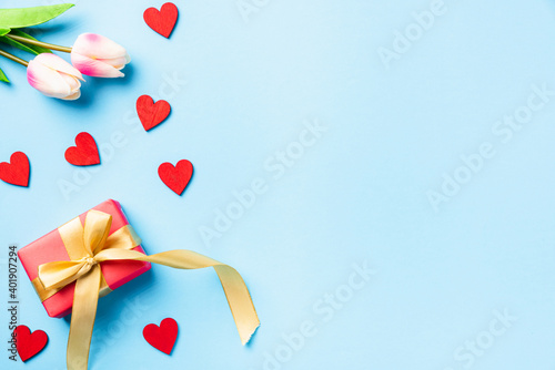 Happy Valentines' day background concept. Red gift box with a golden bow ribbon and wood red hearts composition greeting card for love isolated on blue background with copy space. Top View from above