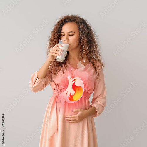 Pregnant African-American woman drinking milk to relieve heartburn on grey background