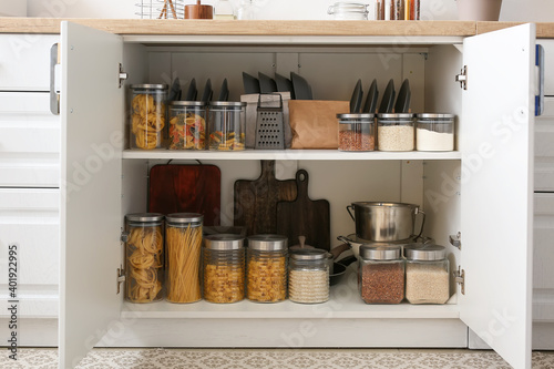 Shelves with utensils and glass jars with products in cupboard