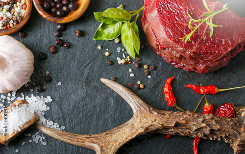 Raw steak meat from roe deer on the bridlic chopping board with ingredients as a sea salt, pepper ,basil,chilli and other. Roe deer antler as a decoration.