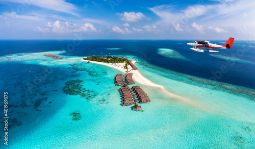 A seaplane is approaching a tropical paradise island in the Maldives with turquoise sea and sunshine