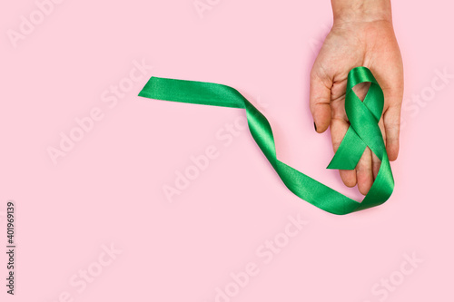 Mujer sosteniendo una cinta verde sobre un fondo de color rosa liso y aislado. Vista superior. Copy space. Concepto: Concienciación sobre el cáncer de riñones