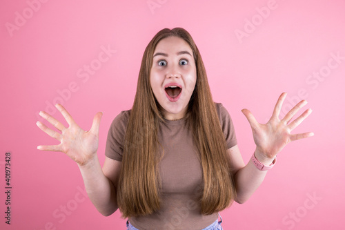 Image of surprised screaming young woman standing over isolated pink background.