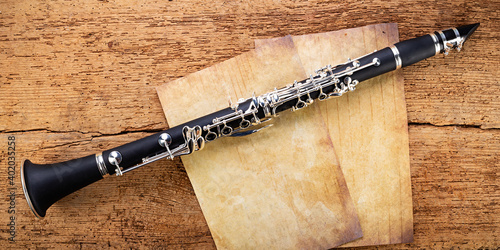 black wooden clarinet silver woodwind musical brass instrument with old empty vintage music sheet copy space paper on retro oak wood background. classic orchestra symphony background.