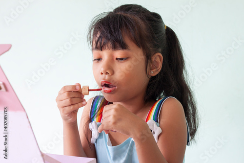 Asian little girl holds a lip gloss in hand paint her labia is learning use cosmetic by herself.