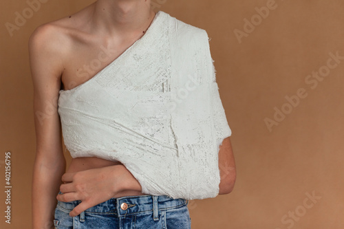 Yuong boy on a beige isolated background with a back, collarbone or shoulder injury. Medical care for fracture of the clavicle.