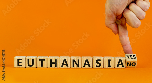 Euthanasia yes or no symbol. Male hand turns cubes and changes words 'Euthanasia yes' to 'Euthanasia no'. Medical and euthanasia yes or no concept. Beautiful orange background, copy space.