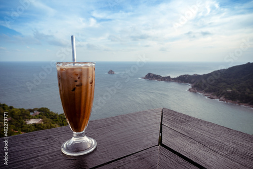 iced latte coffee glass on wooden table terrace with sea view from mountain peak