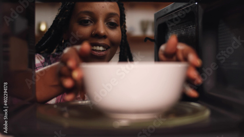 African woman reheat food in ceramic bowl using microwave oven