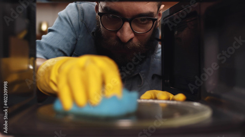 Bearded man in eyeglasses cleaning microwave oven in kitchen