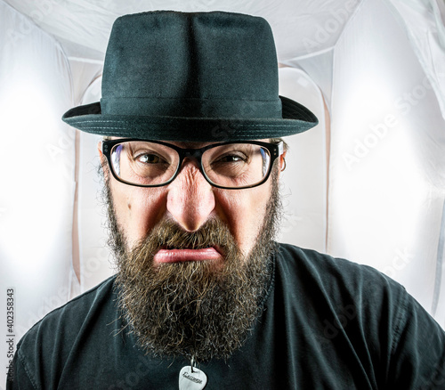 A bearded and angry looking man with black glasses and hat