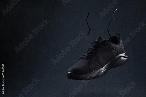Fashion black unbranded sneaker with laces flying on dark background. Black sport running shoes levitate in air.