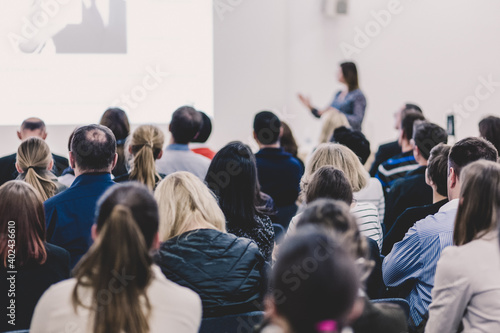 Business and entrepreneurship symposium. Female speaker giving a talk at business meeting. Audience in conference hall. Rear view of unrecognized participant in audience. Copy space on whitescreen.