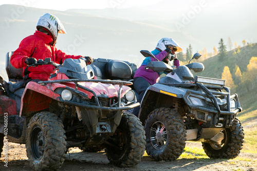 Happy drivers in protective helmets enjoying extreme ride on ATV quad motorbikes in fall mountains at sunset.