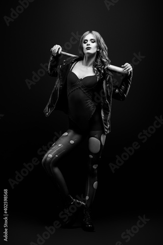 Monochrome studio portrait of young beautiful woman in a leather jacket, red underwear Looks into the camera and beats a wooden baseball bat