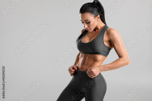 Fitness woman showing abs and flat belly, on gray background. Beautiful athletic girl, shaped abdominal