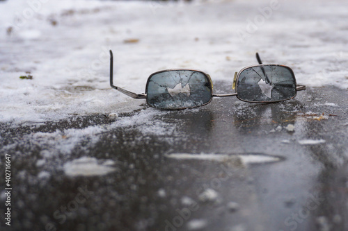 Broken glasses lie in the snow near an icy path. Concept about the danger of slipping and falling on icy paths in winter.