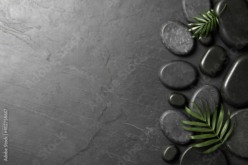 Spa stones and green leaves on black table. Space for text