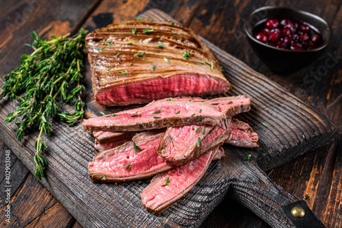 Barbecue sliced flank beef meat steak on a wooden cutting board. Dark wooden background. Top view