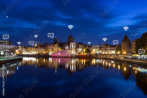 Motlawa River and lit old buildings on the Long Bridge waterfront at the Main Town (Old Town) in Gdansk, Poland, at dusk. Wireless network connection, WiFi, smart city and online messaging concept. 