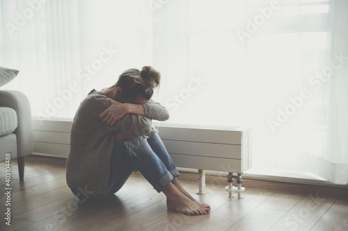 A lonely young woman feels depressed and stressed as she sits on the floor with her head in her hands. Negative emotions and mental health concept.