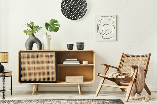 Stylish scandinavian living room interior of modern apartment with wooden commode, design armchair, carpet, leaf in vase, table lamp and personal accessories in unique home decor. Template.