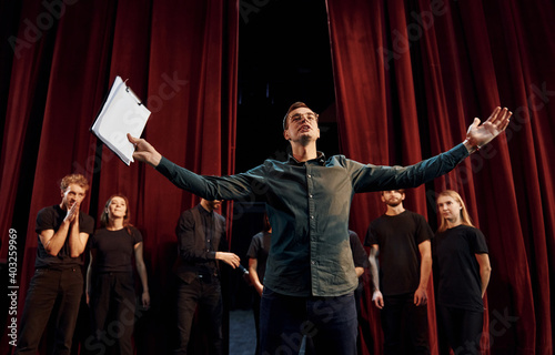 Man is practicing his role. Group of actors in dark colored clothes on rehearsal in the theater