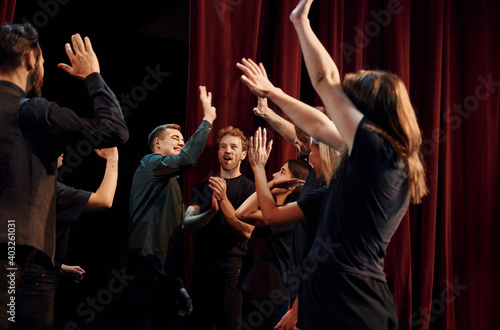 Giving high five, celebrating success. Group of actors in dark colored clothes on rehearsal in the theater
