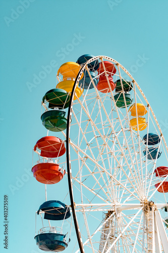 Ferris wheel booths on a blue sky background on a sunny day. Colorful bright cabin of the Ferris wheel against the sky. Fun high rides of green, yellow, blue and red colors in the park in summer.