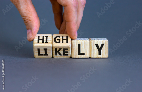 Highly likely symbol. Hand turns the wooden cube with words 'Highly likely' on a beautiful grey background. Business and highly likely concept. Copy space.