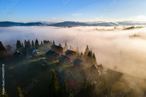 Aerial view of a village houses on hill top in autumn foggy mountains at sunrise.