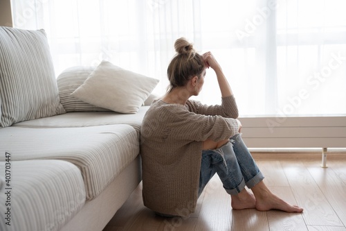 A depressed woman is sitting on the floor in the living room. Sorrow and regret.