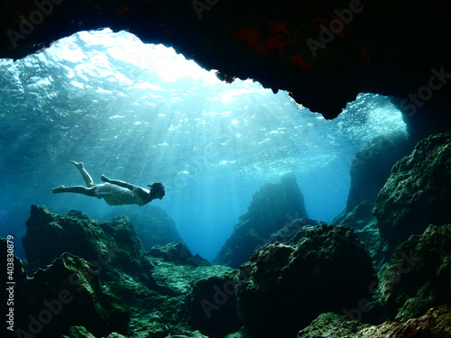 woman lady free diving apnea underwater cave sun beams and rays ocean scenery with human