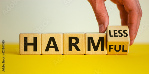 From harmful to harmless. Male hand turns the cube and changes word 'harmful' to 'harmless'. Beautiful yellow table, white background. Business and harmful or harmless concept. Copy space.